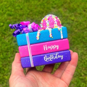 May include: A stack of three wooden boxes decorated with colorful sprinkles and glitter. The top box has a pink and white ice cream cone with white frosting dripping down the sides. The middle box says "Happy" in white letters. The bottom box says "Birthday" in white letters.
