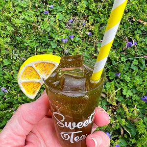 May include: A miniature glass of iced tea with a lemon wedge and a yellow and white striped straw. The glass has the words "Sweet Tea" written on it.