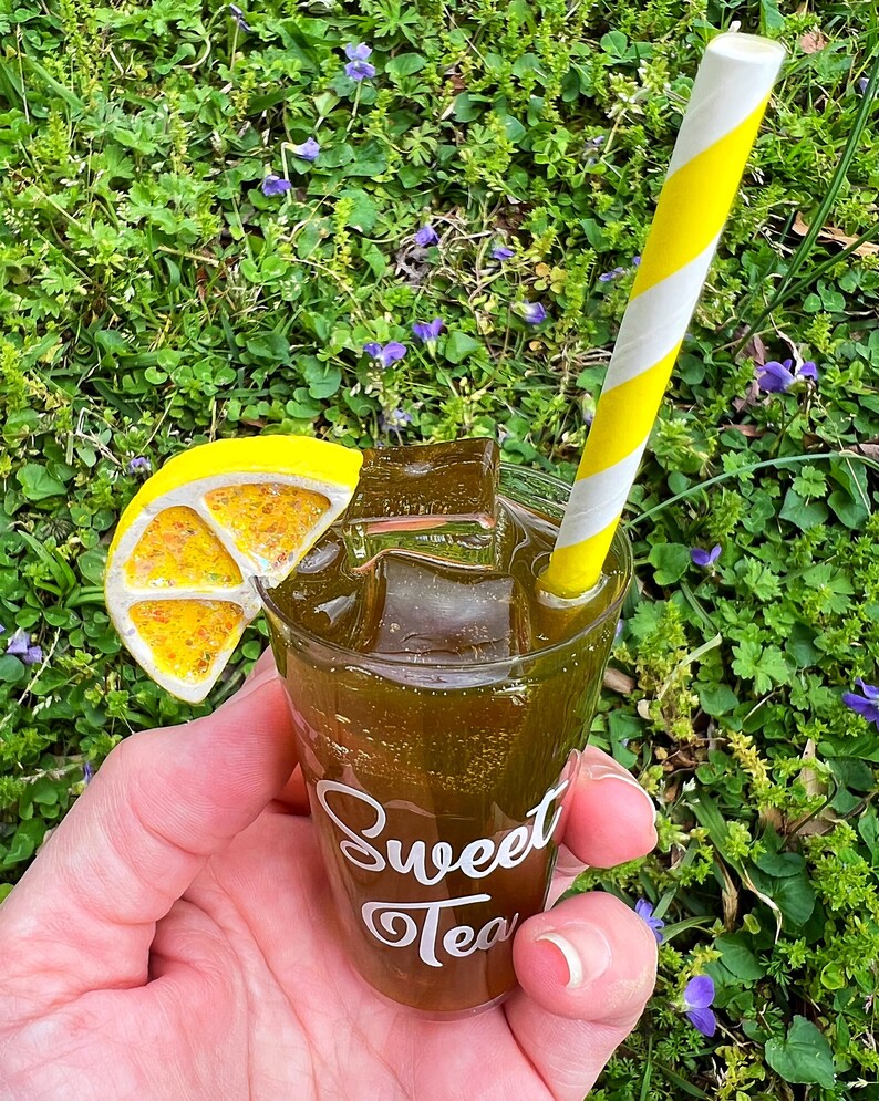 May include: A miniature glass of iced tea with a lemon wedge and a yellow and white striped straw. The glass has the words "Sweet Tea" written on it.