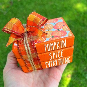 May include: Three wooden blocks stacked on top of each other. The top block has a pumpkin pattern and the text "Pumpkin Spice" printed on it. The middle block has the text "Spice" printed on it. The bottom block has the text "Everything" printed on it. The blocks are tied together with a brown twine bow and a red and orange plaid bow.