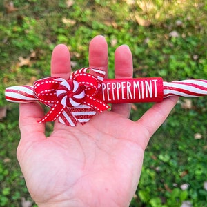 May include: A red and white striped wooden rolling pin with the word "Peppermint" painted on it. The rolling pin is decorated with a red and white peppermint candy and a red bow.