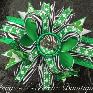May include: A green, black, and white zebra print hair bow with shamrock accents and a green bottle cap with the word "Lucky" on it.