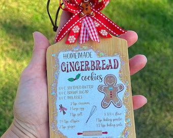 May include: A wooden gingerbread cookie recipe ornament with a red and white checkered ribbon bow. The ornament features a gingerbread man illustration and the text "HOMEMADE GINGERBREAD cookies". The recipe includes ingredients like softened butter, brown sugar, molasses, cinnamon, egg, salt, allspice, and ginger. It also includes baking instructions to bake at 350 degrees Fahrenheit for 8-10 minutes.