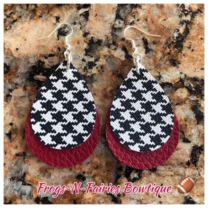 May include: Teardrop earrings with a layered design. The top layer features a black and white houndstooth pattern, while the bottom layer is a textured burgundy. The earrings have silver-colored hooks. The text "Frogs-N-Fairies Bowtique" is visible.