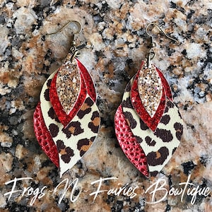 May include: A pair of dangle earrings with three layers of leather. The top layer is gold glitter, the middle layer is red, and the bottom layer is leopard print. The earrings are attached to gold hooks.
