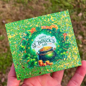 May include: Green and gold glitter card with a shamrock border and the text "Happy St. Patrick's Day". A pot of gold sits in the center of the card.
