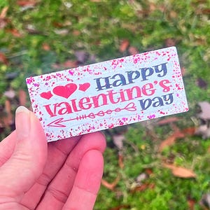 May include: A white card with pink glitter and red hearts that says "Happy Valentine's Day".