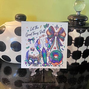 Pode incluir: Impress&atilde;o art&iacute;stica quadrada com tema Mardi Gras. A impress&atilde;o apresenta uma ilustra&ccedil;&atilde;o colorida de uma lagosta, la&ccedil;o, m&aacute;scara e donut. O texto diz "Let The Good Times Roll". A impress&atilde;o &eacute; exibida em um suporte transparente.