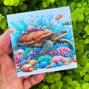 May include: Square tile featuring a vibrant underwater scene with a sea turtle, coral, and fish. The turtle has a brown shell and is surrounded by colorful coral, starfish, and various fish. The background is a light blue with bubbles.