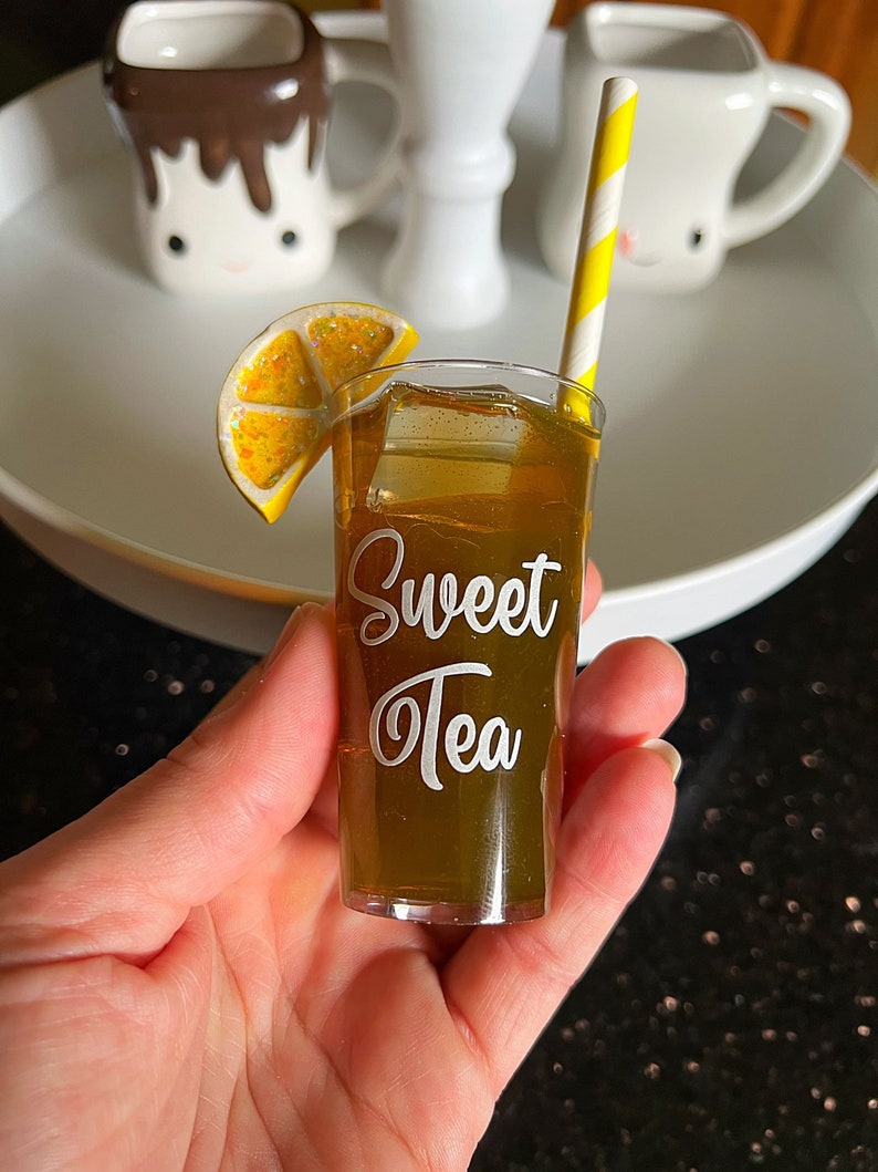 May include: A miniature glass of iced tea with a lemon wedge and a yellow and white striped straw. The glass is labeled "Sweet Tea".