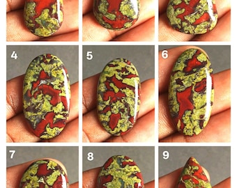 Könnte beinhalten: Neun polierte Edelsteine mit roten, grünen und gelben Mustern. Die Steine haben verschiedene Formen, darunter Tropfen und Oval, und werden vor einem neutralen Hintergrund gezeigt. Die Edelsteine sind wahrscheinlich für die Schmuckherstellung oder das Sammeln gedacht.