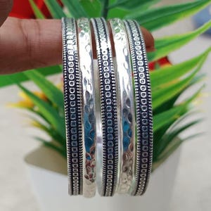 Könnte beinhalten: Eine weiße Keramik-Tasse mit schwarzem Henkel und dem Text "But First, Coffee" in fetter, schwarzer Schrift. Die Tasse steht vor einem verschwommenen Hintergrund, der eine gemütliche Umgebung suggeriert.