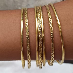 May include: Several gold bangles are displayed on an arm. Some are plain, while others have an etched design. The bangles' metallic sheen is highlighted. The jewellery is a classic accessory, suitable for various occasions. The bangles are a timeless fashion item.