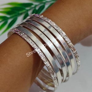 Könnte beinhalten: Ein Satz von sechs silbernen Armreifen. Die Armreifen sind glatt und poliert, mit floralen Mustern an den Rändern. Der Text "Shree Jaipur Silver" ist auf dem Bild sichtbar.