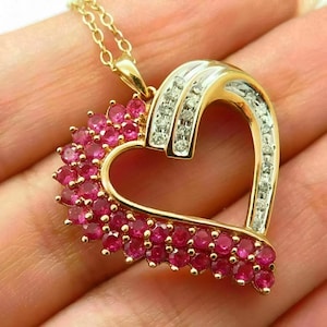 May include: A gold-toned heart pendant necklace. The heart is outlined with gold and filled with small, round, pink gemstones. The top arch of the heart is encrusted with small, clear gemstones. The necklace chain is also gold.