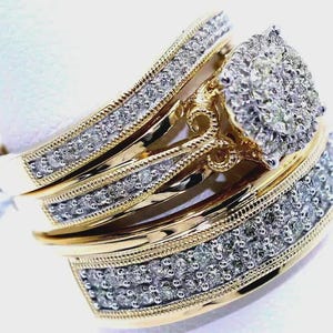 May include: A set of three gold rings with a diamond cluster and diamond accents. The rings have a gold band with a row of small diamonds and a textured edge. The center ring features a large cluster of diamonds.