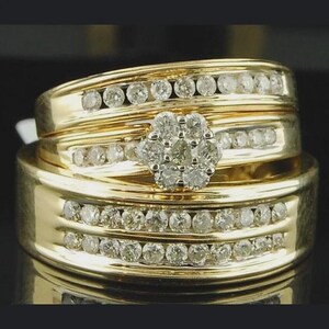 May include: A set of three gold wedding rings. The rings are adorned with multiple small, round diamonds. The largest ring features a cluster of diamonds in a floral arrangement. The bands have a polished finish, reflecting light.