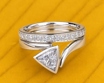 May include: A silver-toned ring set consisting of two bands. The top band features a row of small, clear, round-cut stones. The bottom band has a smooth, polished finish and a single, prominent, triangular-cut clear stone in a bezel setting.