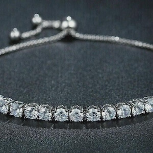 May include: A silver bracelet featuring a line of clear, round gemstones. The bracelet has a fine chain and a sliding clasp for adjustable sizing. The gemstones are set close together, creating a continuous sparkle.