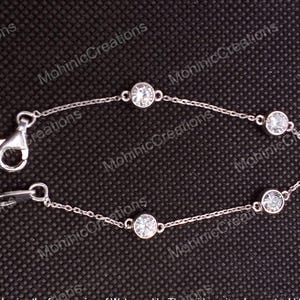 May include: A delicate silver bracelet with five clear, round gemstones set along a fine chain. The bracelet has a lobster clasp. The background is a dark, textured surface.