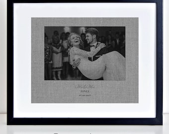 May include: Black and white photo of a couple dancing at their wedding reception. The bride is being held in the groom's arms. The photo is printed on a grey linen background with the text "Mr. & Mrs. Jones 07.30.2017" printed below the photo.