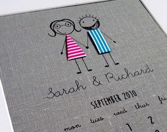 Puede incluir: Una impresión enmarcada de un calendario gris con figuras de palitos tomados de la mano sobre el texto "Sarah & Richard" y el mes "Septiembre de 2010". La fecha "25" está resaltada con un corazón. El calendario está en un marco blanco.