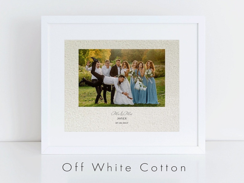 May include: A framed wedding photograph of a bride and groom with their wedding party. The photograph is printed on off-white cotton canvas and features a rustic, textured background. The text "Mr. & Mrs. JONES 07.10.2017" is printed below the photograph.