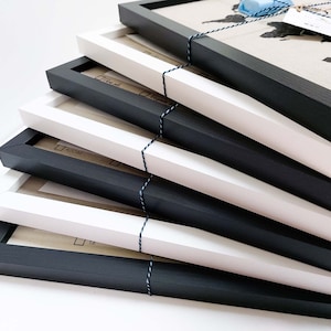 May include: A stack of six picture frames, alternating between black and white frames. The frames are made of wood and have a simple, modern design.