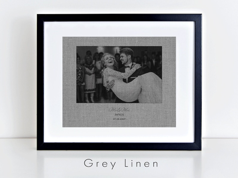 May include: Black and white photograph of a couple dancing at their wedding reception. The photo is printed on a grey linen canvas and framed in a black frame. The text "Mr. & Mrs. Jones 07.10.2017" is printed below the photo.