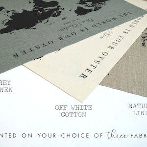 May include: Three fabric swatches: grey linen, off-white cotton, and natural linen. Each swatch features a world map design with the text "The world is your oyster" printed on it. The text "The world is our oyster" is also printed on the grey linen swatch.