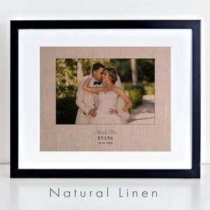 May include: A framed photograph on natural linen with a black frame. The photograph shows a couple kissing. The text below the photograph reads "Mr. & Mrs. Evans 10.01.2012".