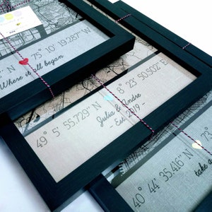 May include: Three framed maps with black frames and white string. Each map has a different location with coordinates and a personalised message. The first map says "Where it all began" with coordinates 75&deg; 10' 19.287" W. The second map says "Julia & Andre - Est. 2019 -" with coordinates 49&deg; 5' 55.729" N and 8&deg; 23' 50.502" E. The third map says "take a" with coordinates 40&deg; 44' 35.416" N.