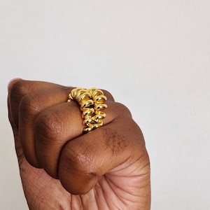 May include: A gold ring with a spiral design is held in a fist. The ring is made of multiple connected coils. The text "Double Fry, No Salt" is at the top of the image.