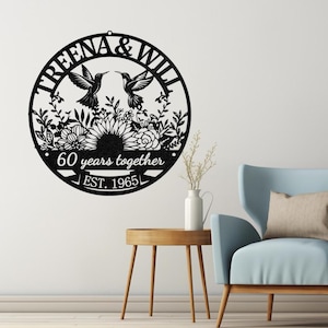 May include: Black metal wall art featuring a circular design with the names "TREENA & WILL" and two hummingbirds facing each other. The design includes floral elements and the text "60 years together EST. 1965".