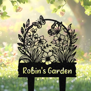Puede incluir: Estaca de jardín de metal negro con diseño floral y de mariposas. La estaca tiene un letrero rectangular con el texto "Robin's Garden" en fuente amarilla. El diseño incluye flores, hojas y mariposas, ideal para la decoración exterior.