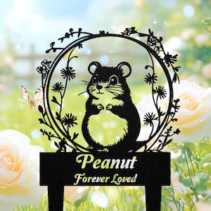 May include: Black metal garden stake featuring a hamster design within a floral wreath. The stake includes the text "Peanut Forever Loved". The background shows a butterfly and white roses.