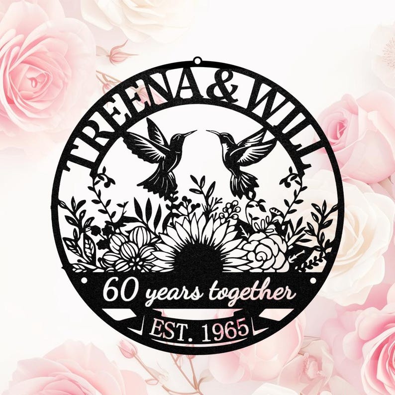 May include: Black metal wall art featuring two hummingbirds facing each other above a floral design. The circular piece includes the names "TREENA & WILL", "60 years together", and "EST. 1965". The background is a soft pink with rose blossoms.