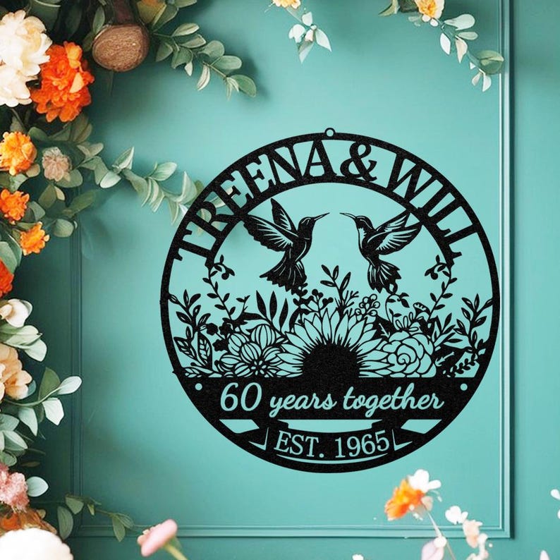 May include: Black metal wall art with the text "TREENA & WILL" and two hummingbirds facing each other. The art also includes the text "60 years together" and "EST. 1965". The art is circular and features floral and leaf designs.