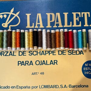 May include: A box of 24 spools of thread labeled "La Paleta Torzal de Schappe de Seda Para Ojal" with the art number 48. The spools are arranged in a row and are in various colors, including white, brown, red, green, blue, and yellow.