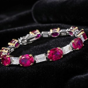 May include: A luxurious bracelet featuring oval-cut ruby gemstones and baguette-cut diamonds. The rubies are a vibrant red, set in gold prongs, and interspersed with the diamonds. The bracelet is displayed against a black background.