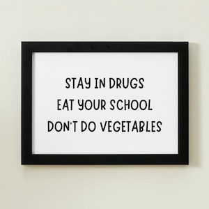 May include: A framed print with the text "STAY IN DRUGS EAT YOUR SCHOOL DON'T DO VEGETABLES" in a black frame. The text is in a bold, sans-serif font, centered on a white background. The frame is rectangular.