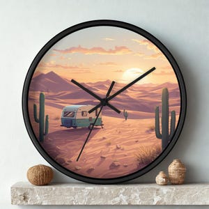Könnte beinhalten: Eine runde Wanduhr mit schwarzem Rahmen und einer Wüstenlandschaft-Illustration. Die Szene zeigt einen hellblauen und weißen Wohnwagen in einer sandigen Wüste mit hohen grünen Kakteen unter einem Himmel bei Sonnenuntergang mit Bergen.