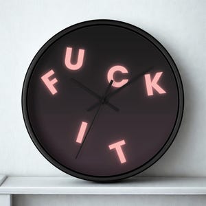 May include: A round black wall clock with the words "FUCK IT" in pink letters. The clock has black hands and a black frame. The background is a gradient of dark purple to black.