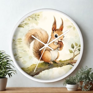 May include: White round wall clock featuring a watercolor illustration of a squirrel holding a nut on a tree branch. The squirrel has brown fur and a fluffy tail. The clock hands are white.