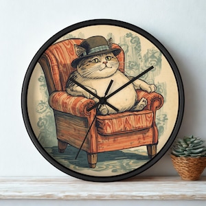 May include: A round wall clock with a black frame featuring an illustration of a round, light-colored cat wearing a dark hat while sitting in an orange and brown striped armchair. The clock face has black hour, minute, and second hands.