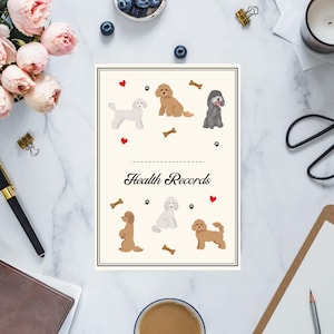 May include: A cream-colored "Health Records" notebook featuring illustrations of various dog breeds, paw prints, and bone graphics. The notebook is surrounded by office supplies, flowers, and a cup of coffee on a marble surface.