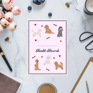 May include: A pink health records booklet with illustrations of various dog breeds, hearts, and bones. The words "Health Records" are written in a cursive font. The booklet is surrounded by office supplies and flowers.