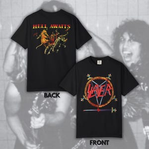 Puede incluir: Una camiseta negra de manga corta mostrada por delante y por detrás. La parte delantera presenta el logo de Slayer en rojo dentro de un pentagrama en llamas con espadas. La parte trasera muestra el texto HELL AWAITS en amarillo y rojo.