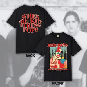 Puede incluir: Camisetas negras con diseños delanteros y traseros. La parte delantera presenta una ilustración de payaso con el texto "ACID BATH" y "WHEN THE KITE STRING POPS". La parte trasera muestra "WHEN THE KITE STRING POPS" en letras rojas.