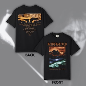Könnte beinhalten: Zwei schwarze T-Shirts mit der Band Bathory. Das vordere Shirt zeigt den Bandnamen und "Twilight of the Gods" über einer Berglandschaft. Das hintere Shirt zeigt den Bandnamen und eine Liste von Songtiteln.